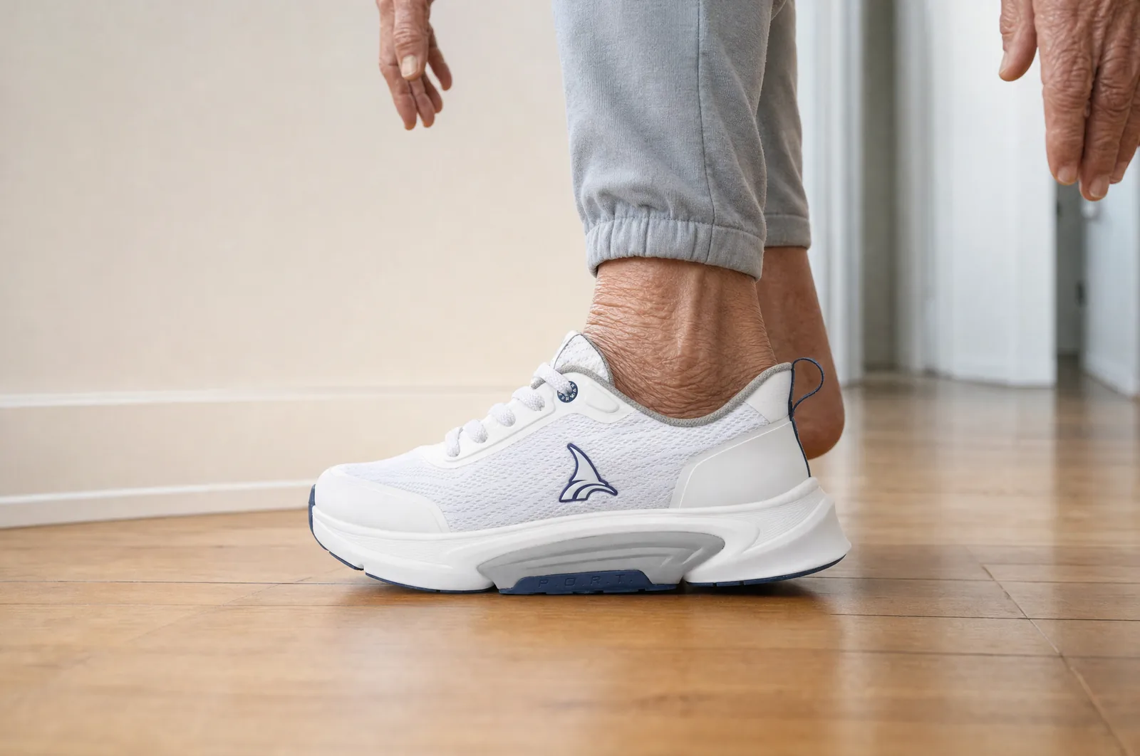 A senior putting the shoe on while standing, no hand on a wall, no chair. The foot going in is the subject. This is the direct answer to card 1 of section 2, so the room should read as the same kind of hallway. Never a fall, a stumble, anyone helping, a cane or a walker.