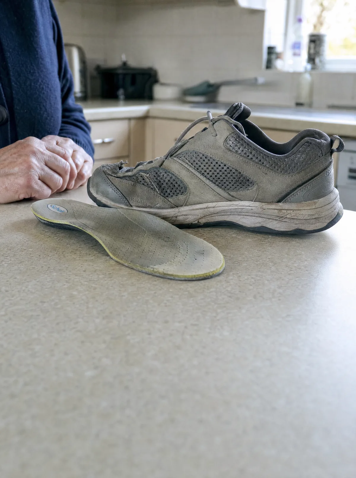 The insert and the cushioned shoe on a kitchen counter, still in reach, clearly used. Hands in frame, no face. Nothing that mocks the attempt: these are reasonable things a reasonable person bought.