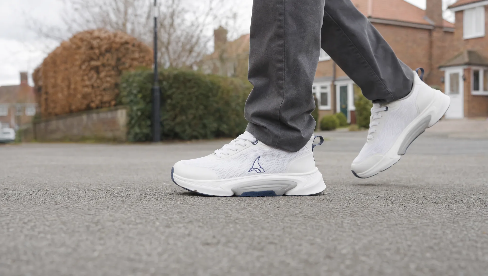 A senior walking on an ordinary residential path, shot wide and low so the sole meets the ground across the frame.